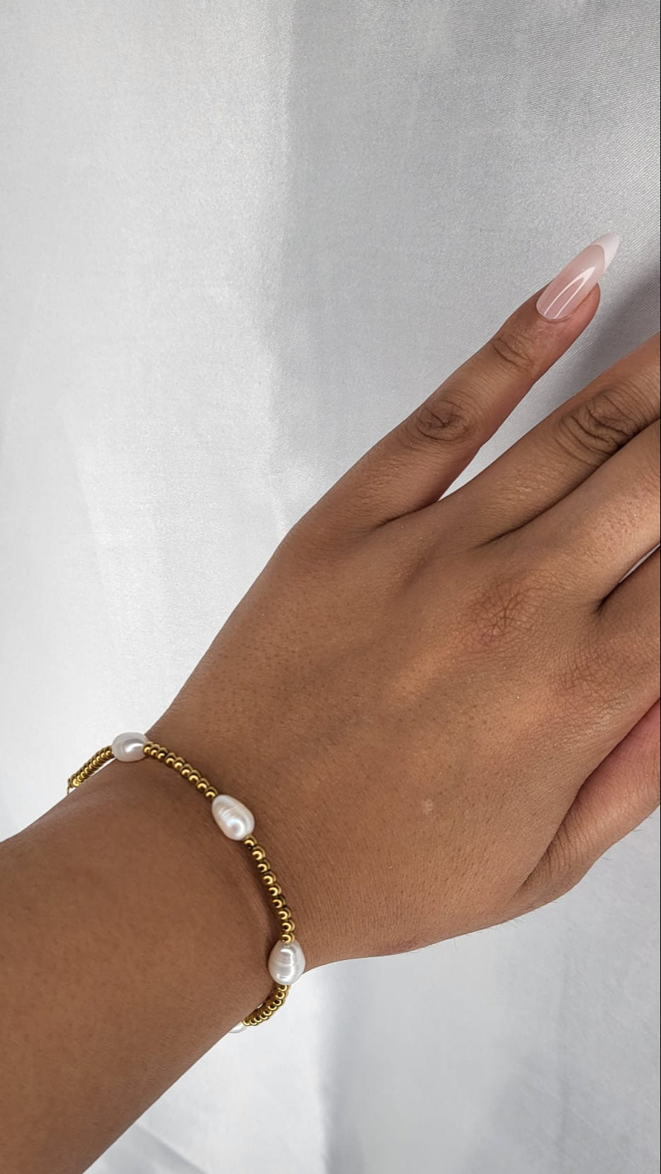 Hand wearing a gold bracelet with pearls on a white background