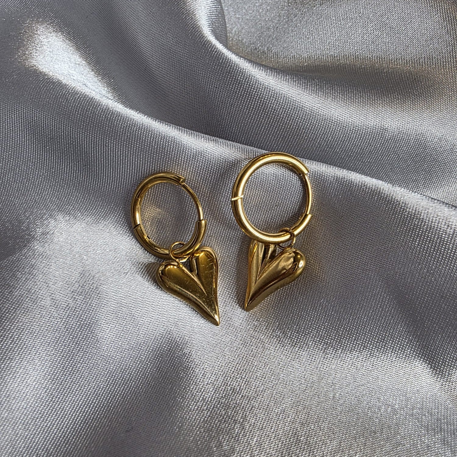 Gold hoop earrings with heart-shaped charms on a gray fabric background