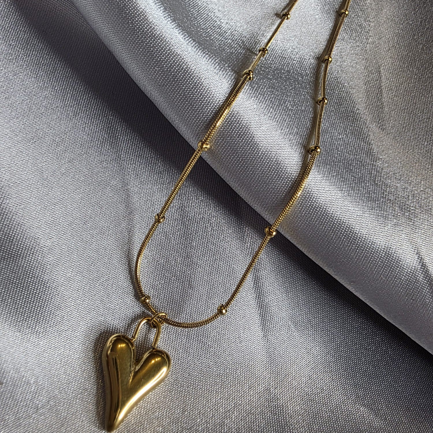 Gold necklace with a heart-shaped pendant on a gray fabric background
