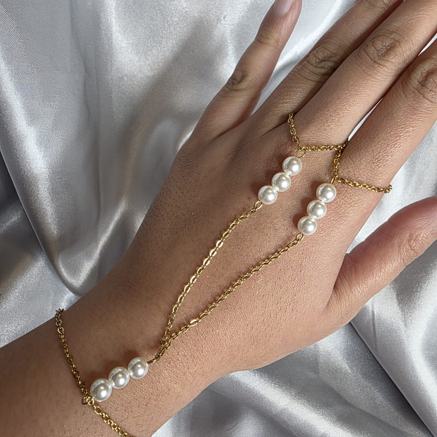 Hand wearing a gold bracelet with pearl beads on a white satin background