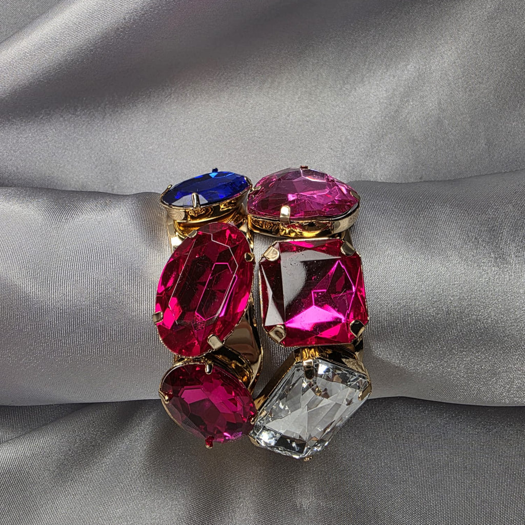 Jewelry with pink, blue, and clear gemstones on a gray fabric background