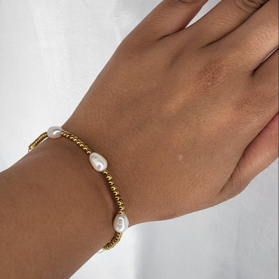 Hand wearing a gold bracelet with pearls on a white background