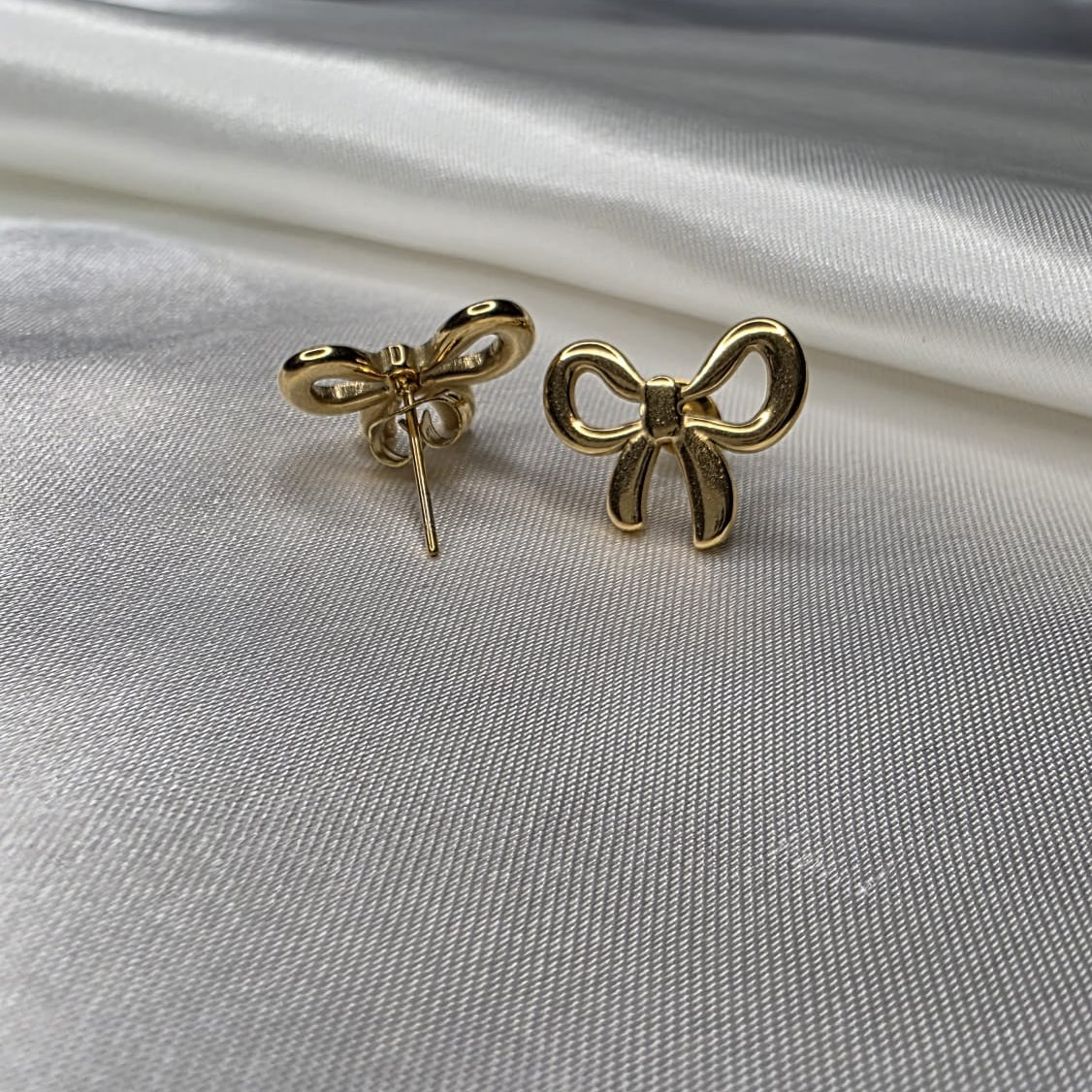 Gold bow-shaped earrings on a white fabric background