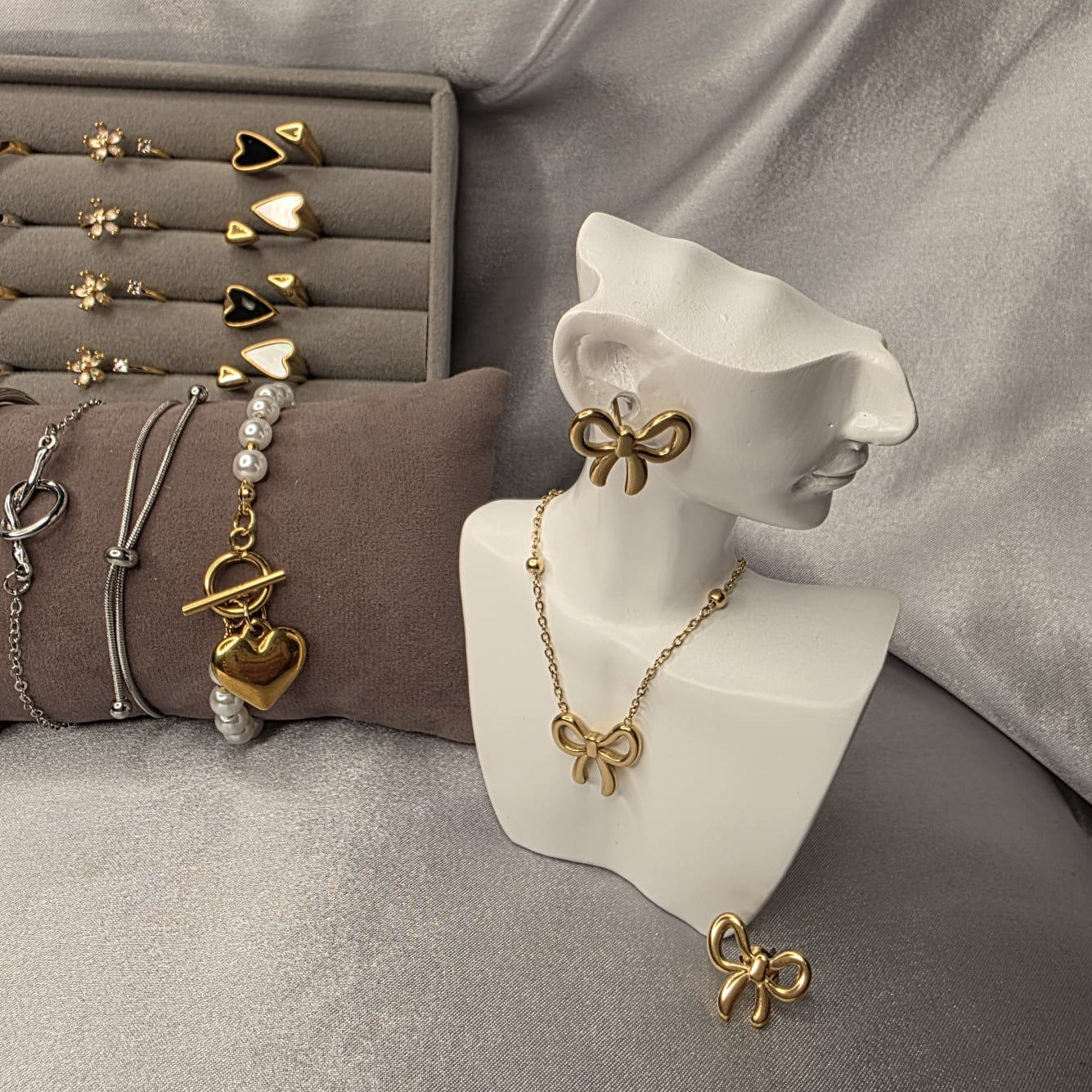 Gold bow-shaped jewelry on a white bust against a gray fabric background