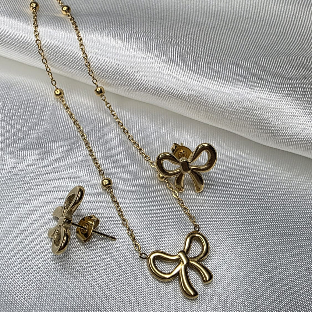 Gold bow-shaped necklace and earrings on a white fabric background