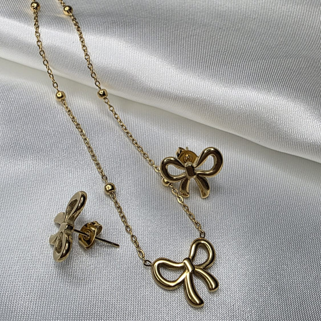 Gold bow-shaped necklace and earrings on a white fabric background