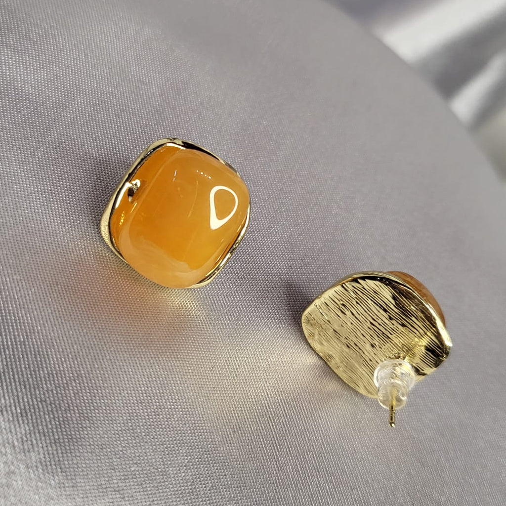 Two gold earrings on a gray fabric background