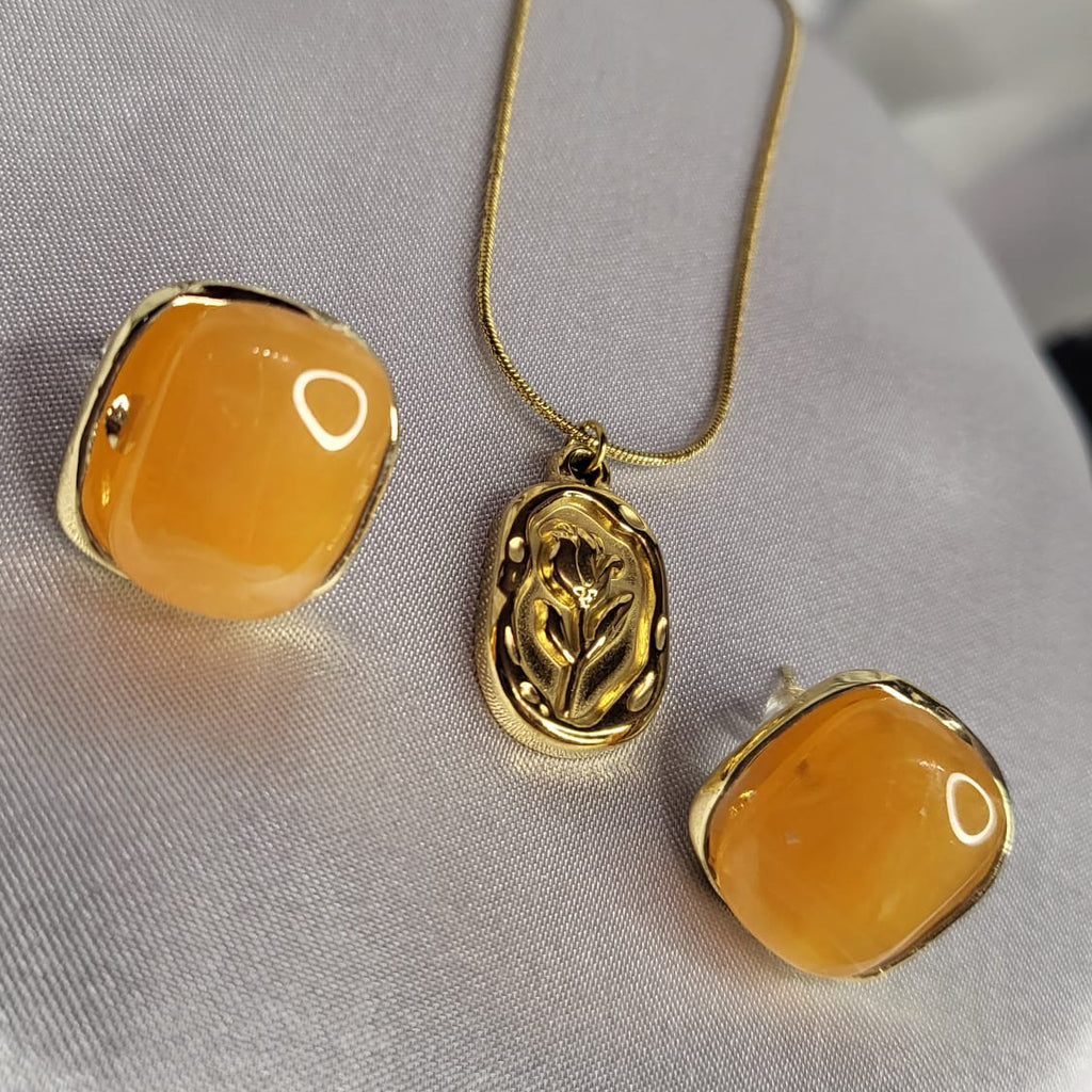 Gold necklace and earrings with orange stones on a silver fabric background