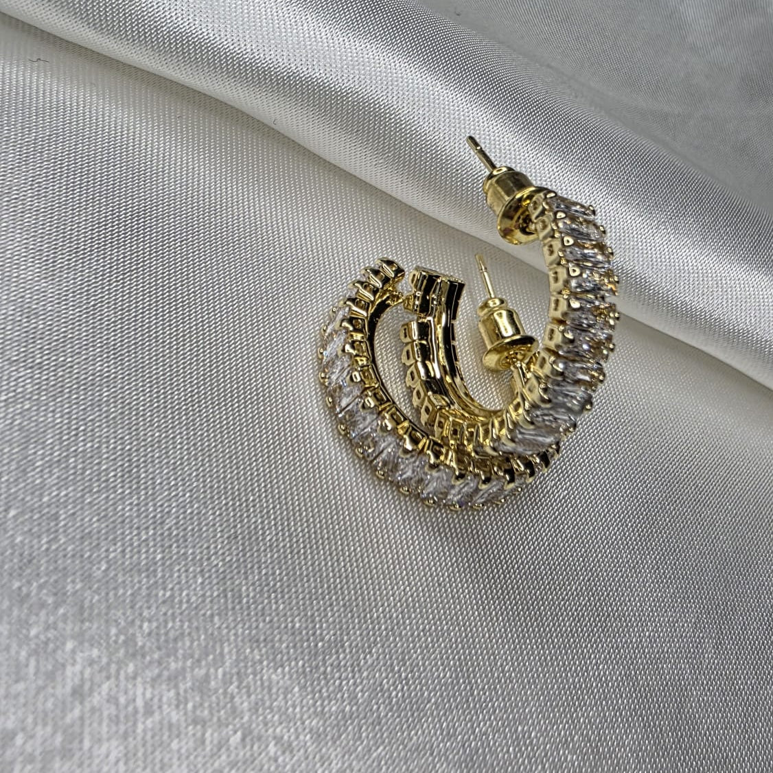 Gold hoop earrings with clear stones on a light gray fabric background