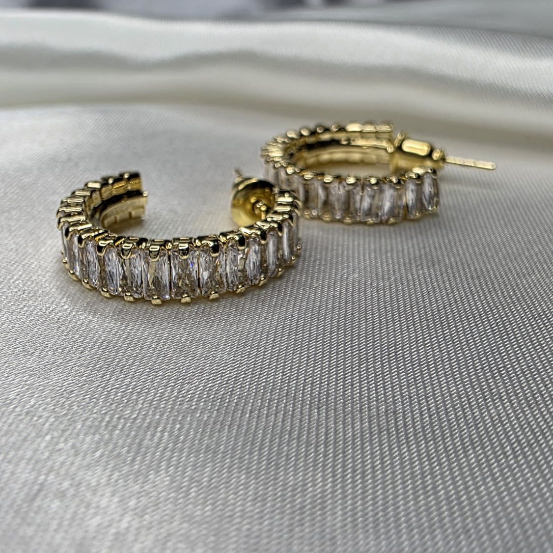 Gold hoop earrings with clear stones on a gray fabric background