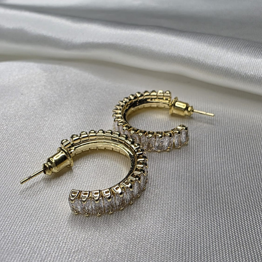 Gold hoop earrings with clear gemstones on a gray fabric background