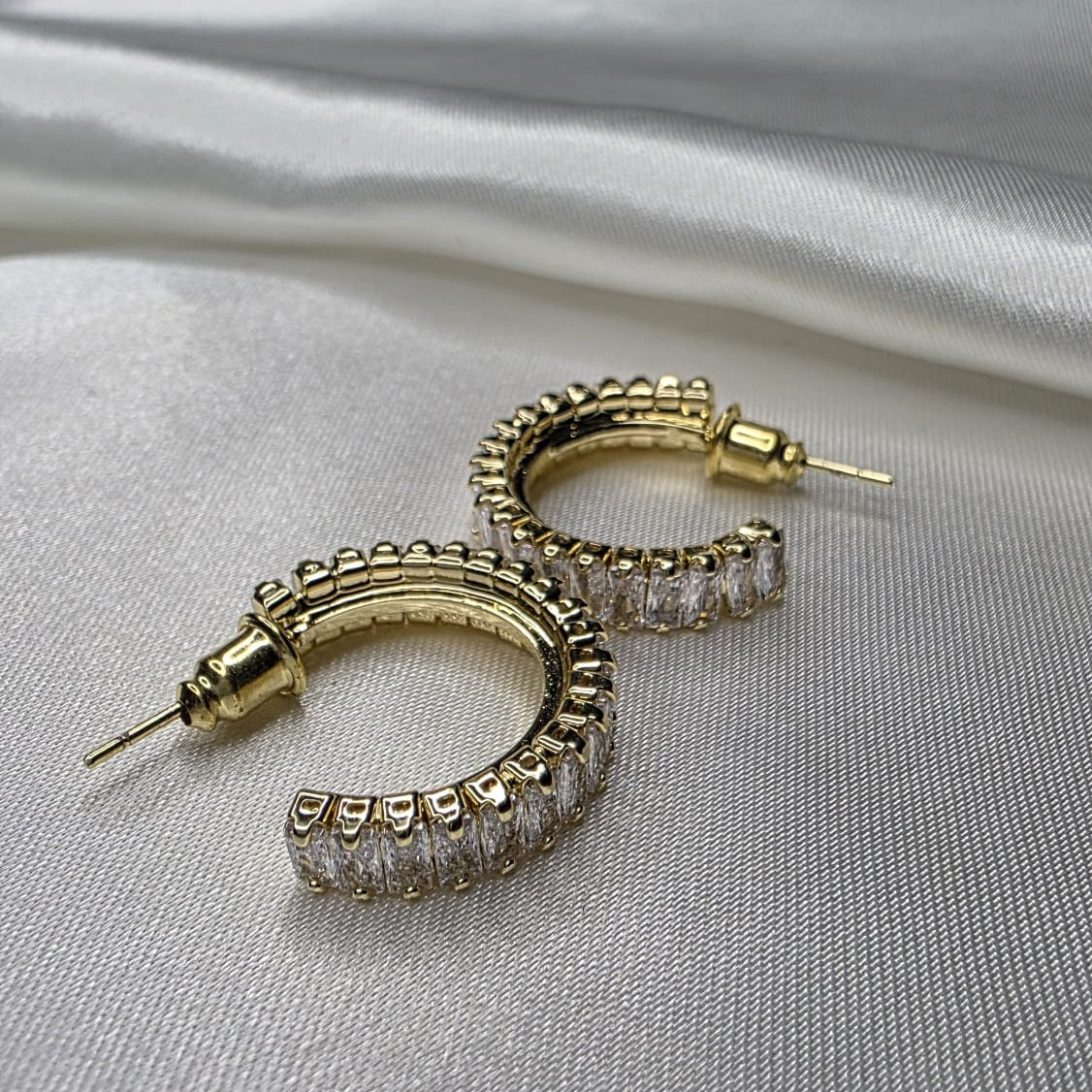 Gold hoop earrings with clear gemstones on a gray fabric background