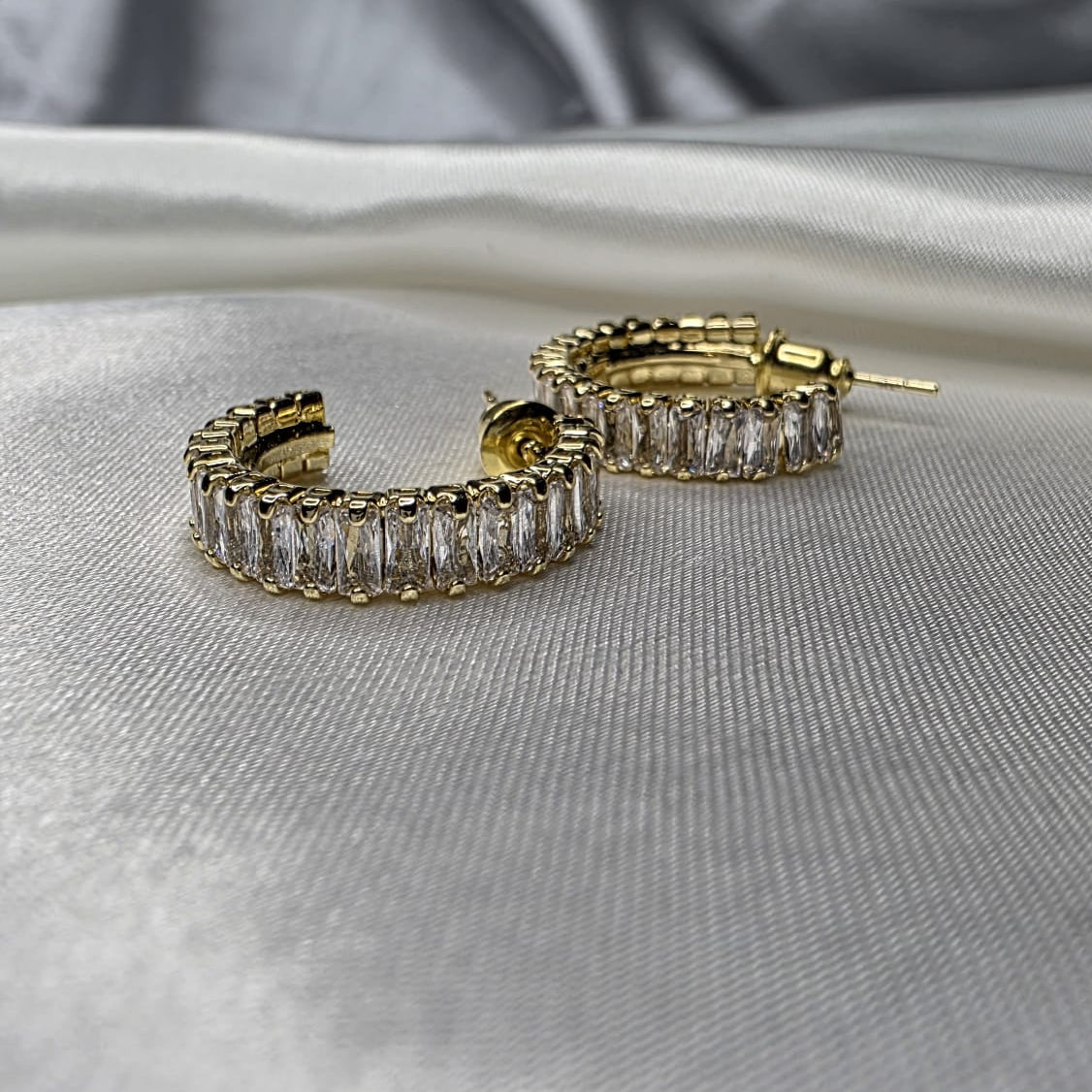 Gold hoop earrings with clear stones on a silver fabric background