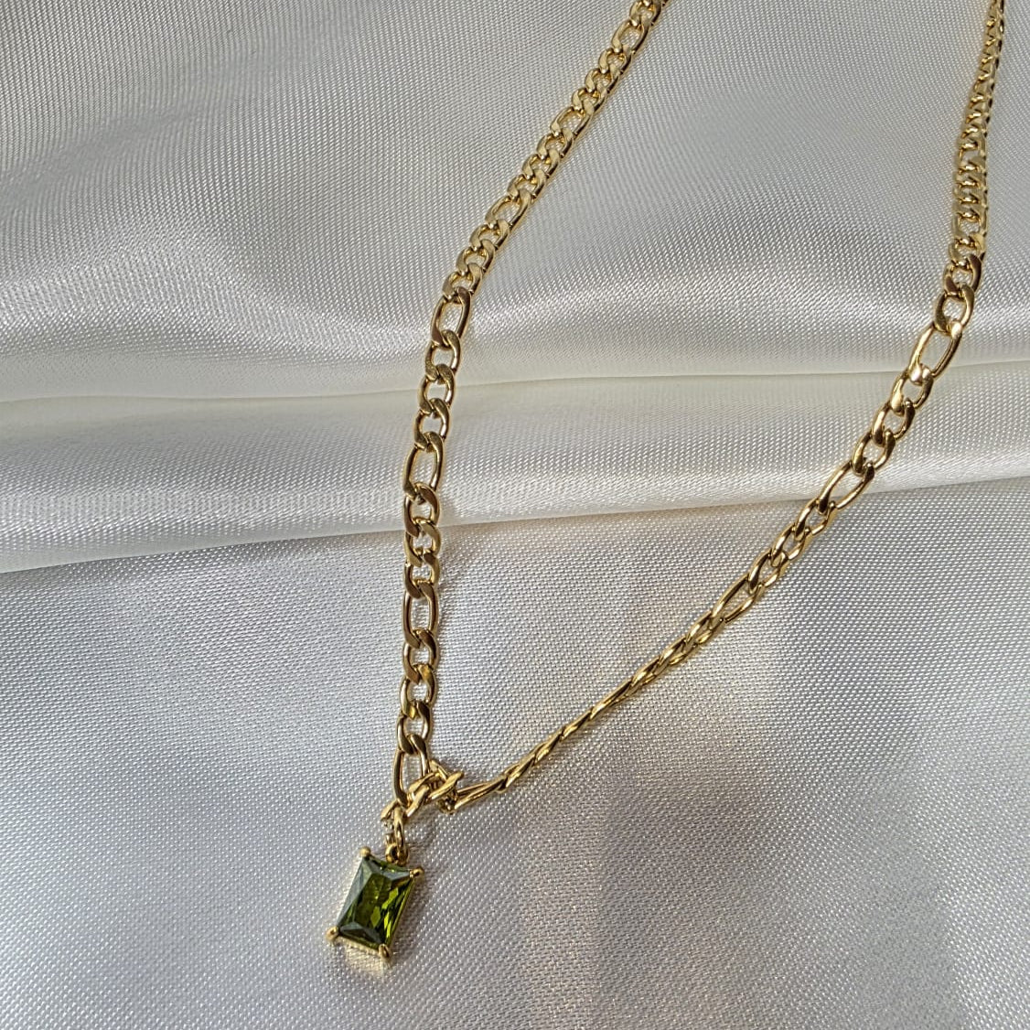 Gold necklace with a green gemstone pendant on a white satin background