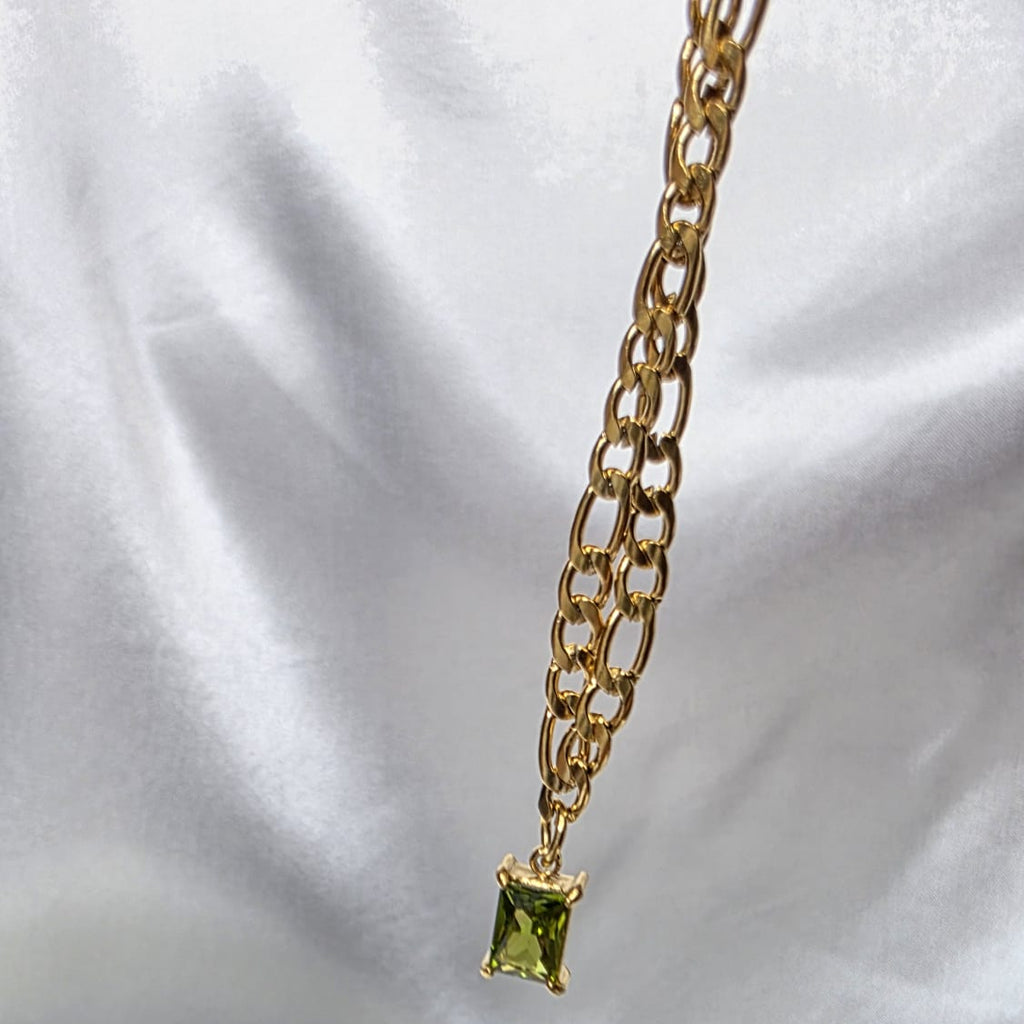 Gold necklace with a green gemstone pendant on a white satin background