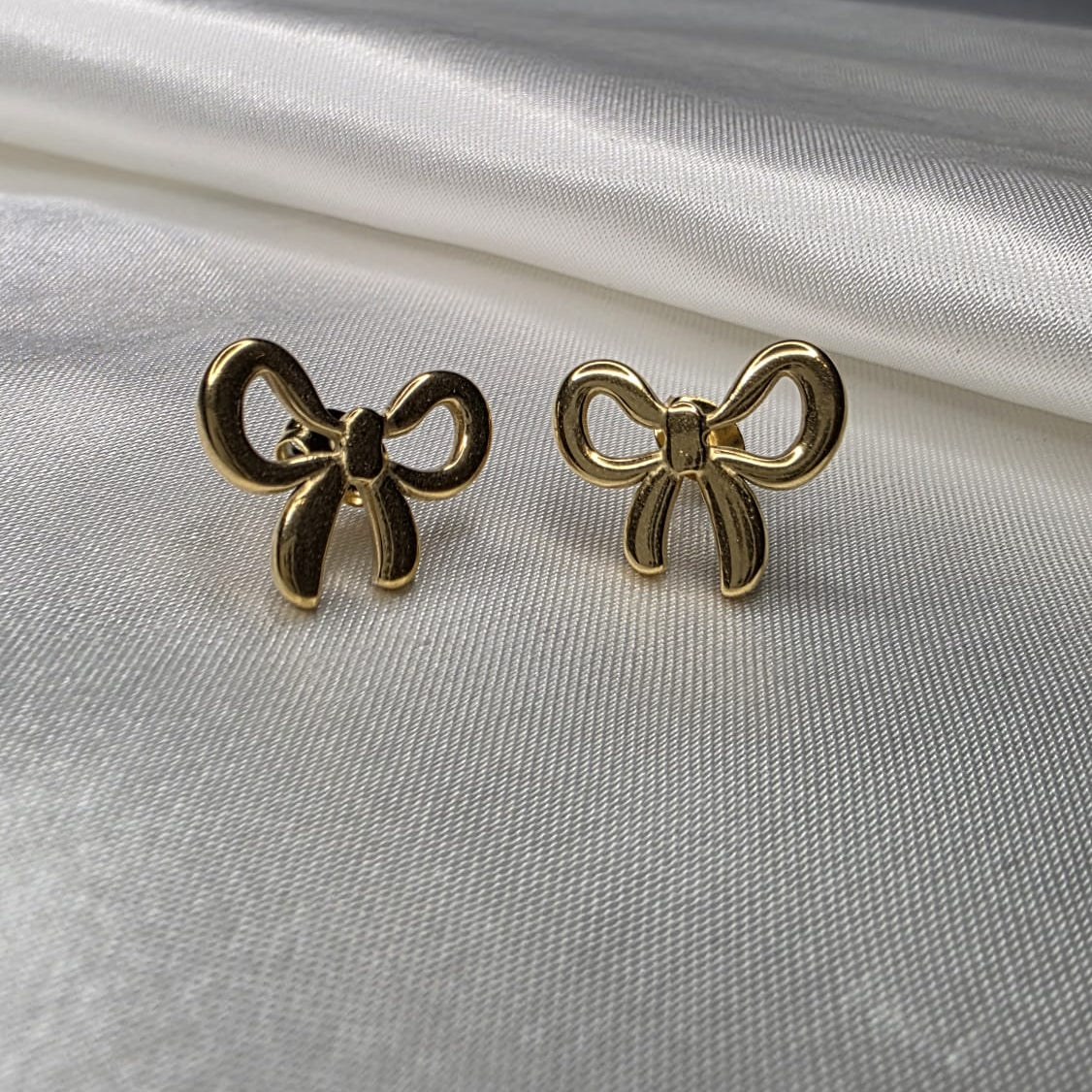 Gold bow-shaped earrings on a white satin background