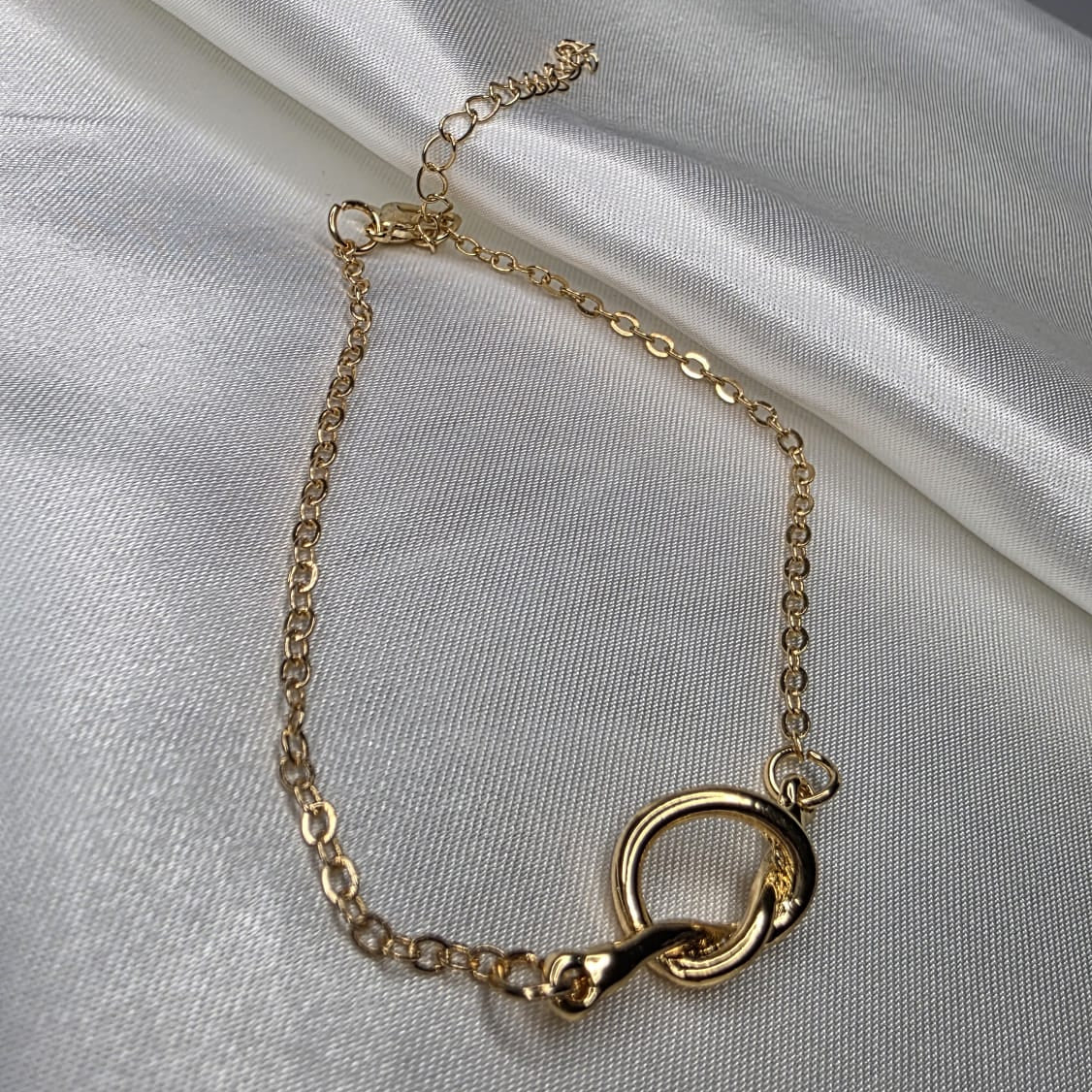 Gold bracelet with a circular clasp on a white fabric background