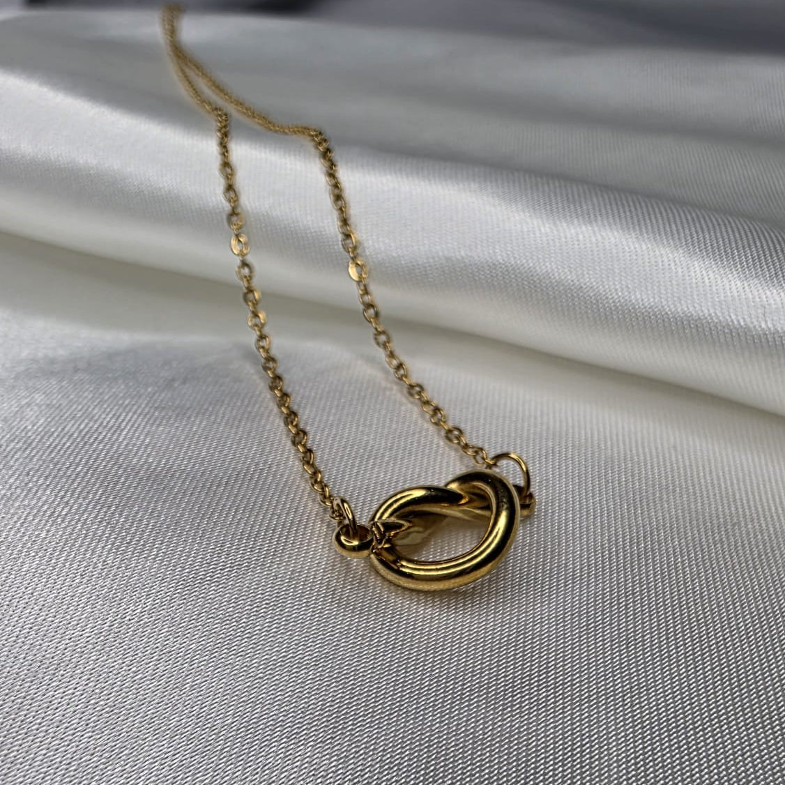 Gold necklace with interlocking rings on a white fabric background