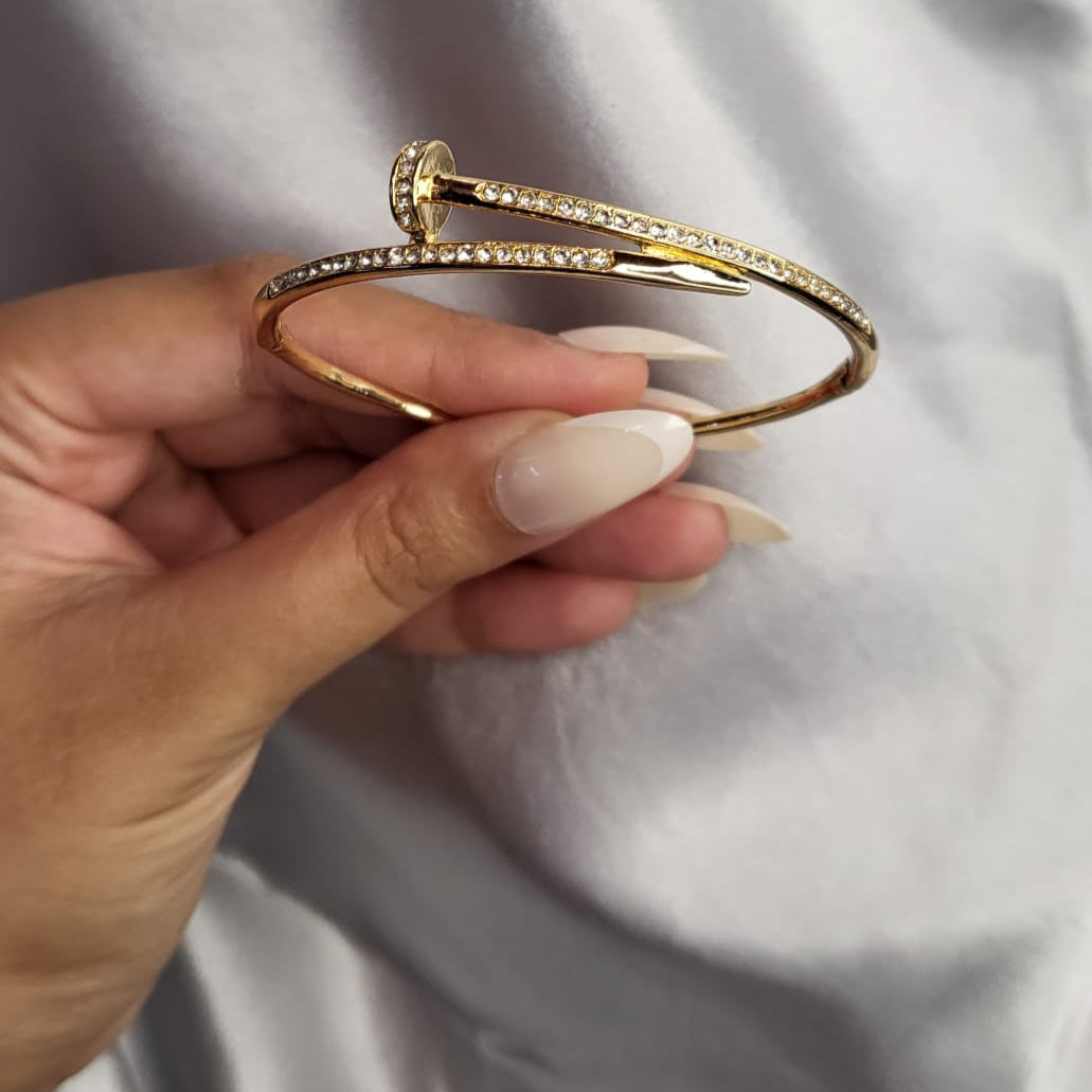 Gold bracelet being held by a hand with light nail polish on a neutral background