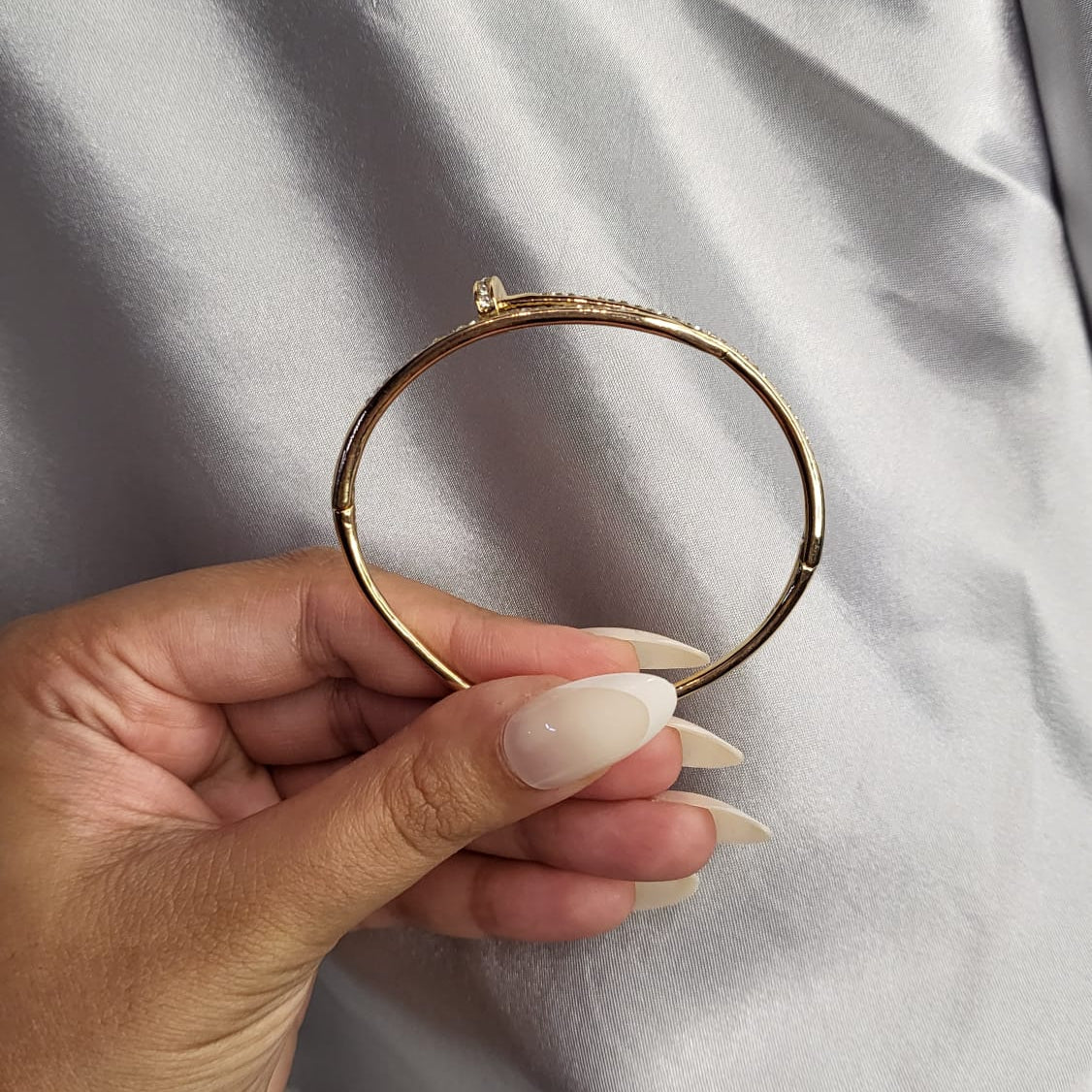 Hand holding a gold bracelet against a plain background