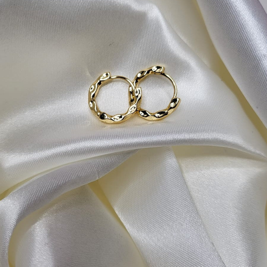 Gold hoop earrings on a white satin surface