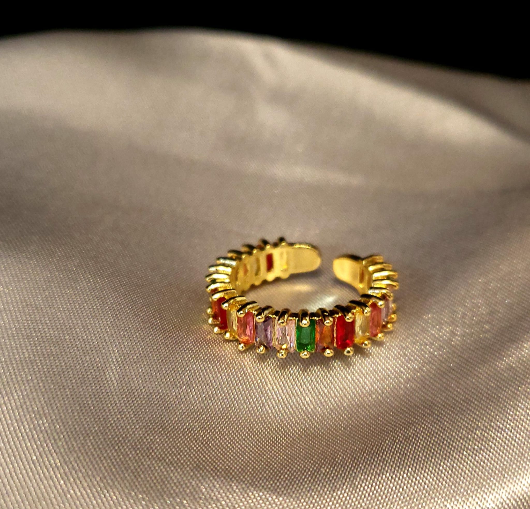 Gold ring with colorful gemstones on a beige fabric background