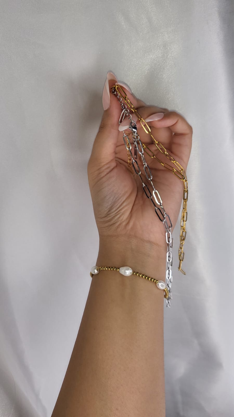 Hand holding gold and silver chain necklaces against a light background