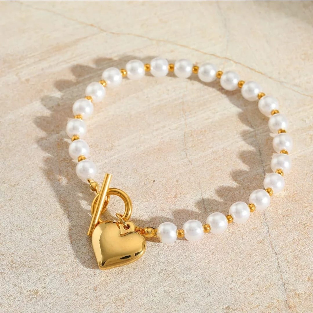 Pearl bracelet with a gold heart lock charm on a beige stone background