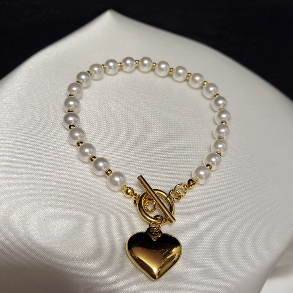 Pearl bracelet with a gold heart charm on a white satin surface