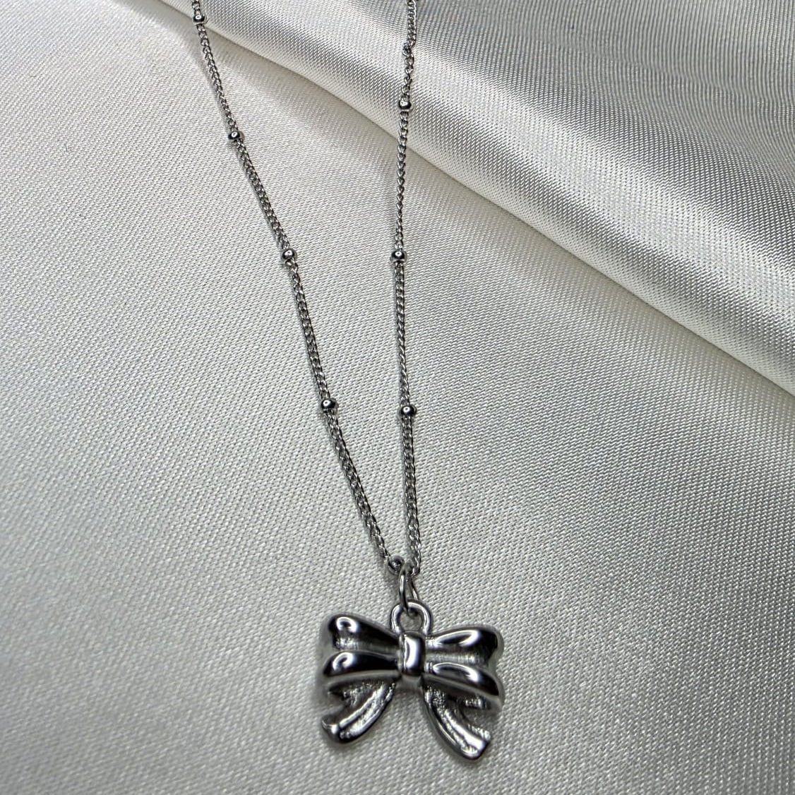 Silver bow-shaped pendant necklace on a light gray fabric background