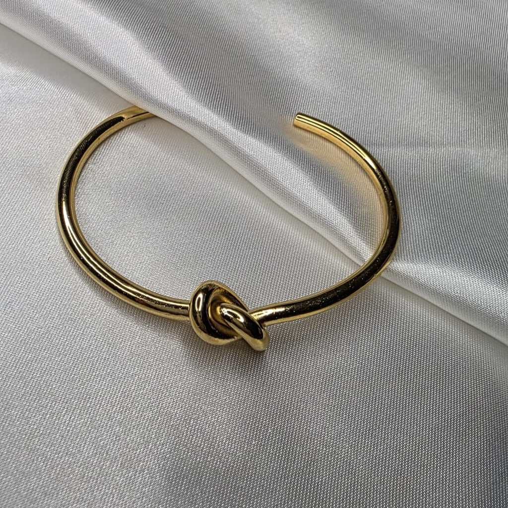 Gold bracelet with a knot design on a white fabric background