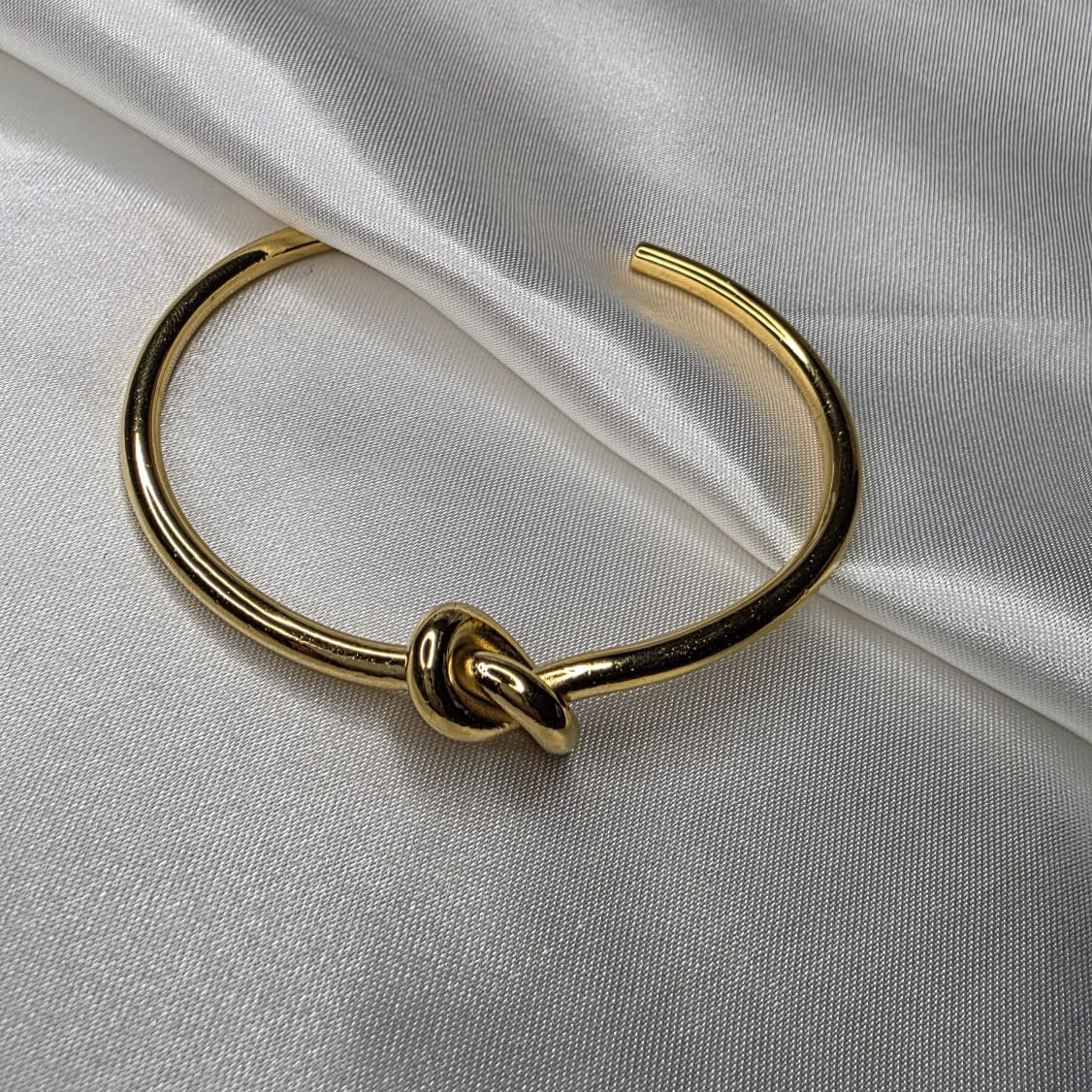 Gold bracelet with a knot design on a white fabric background