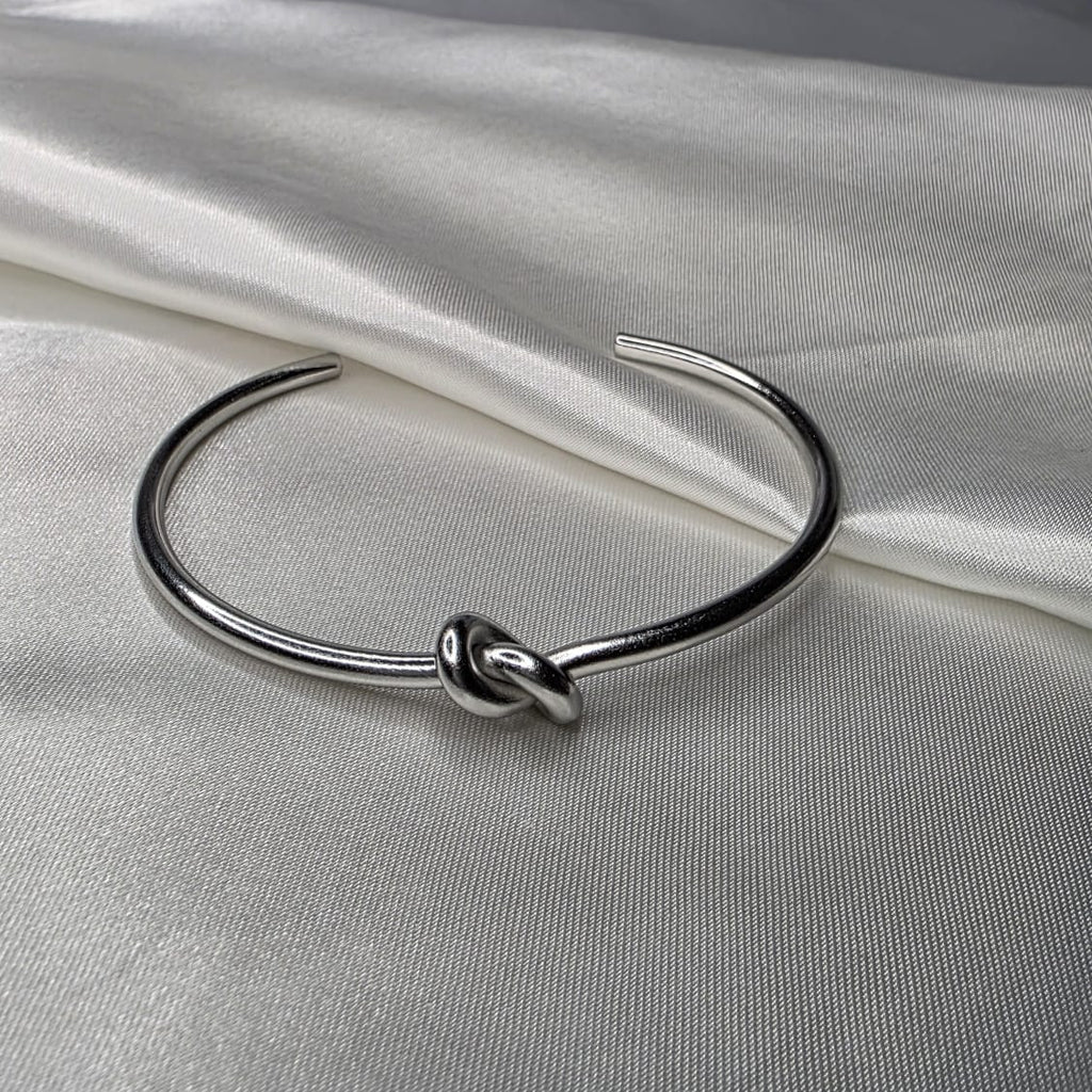 Silver bracelet with a knot design on a white fabric background