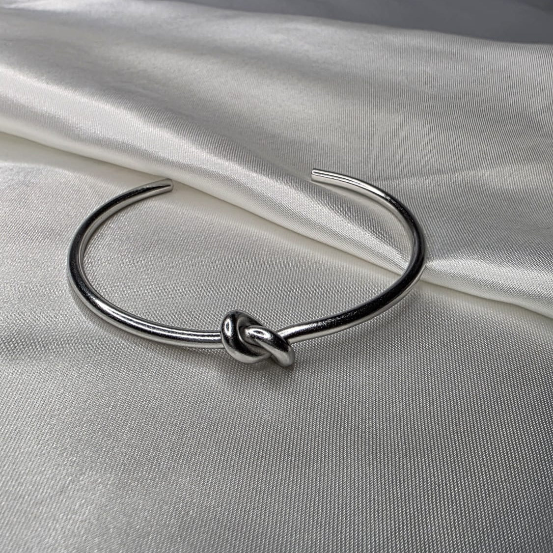 Silver bracelet with a knot design on a white fabric background