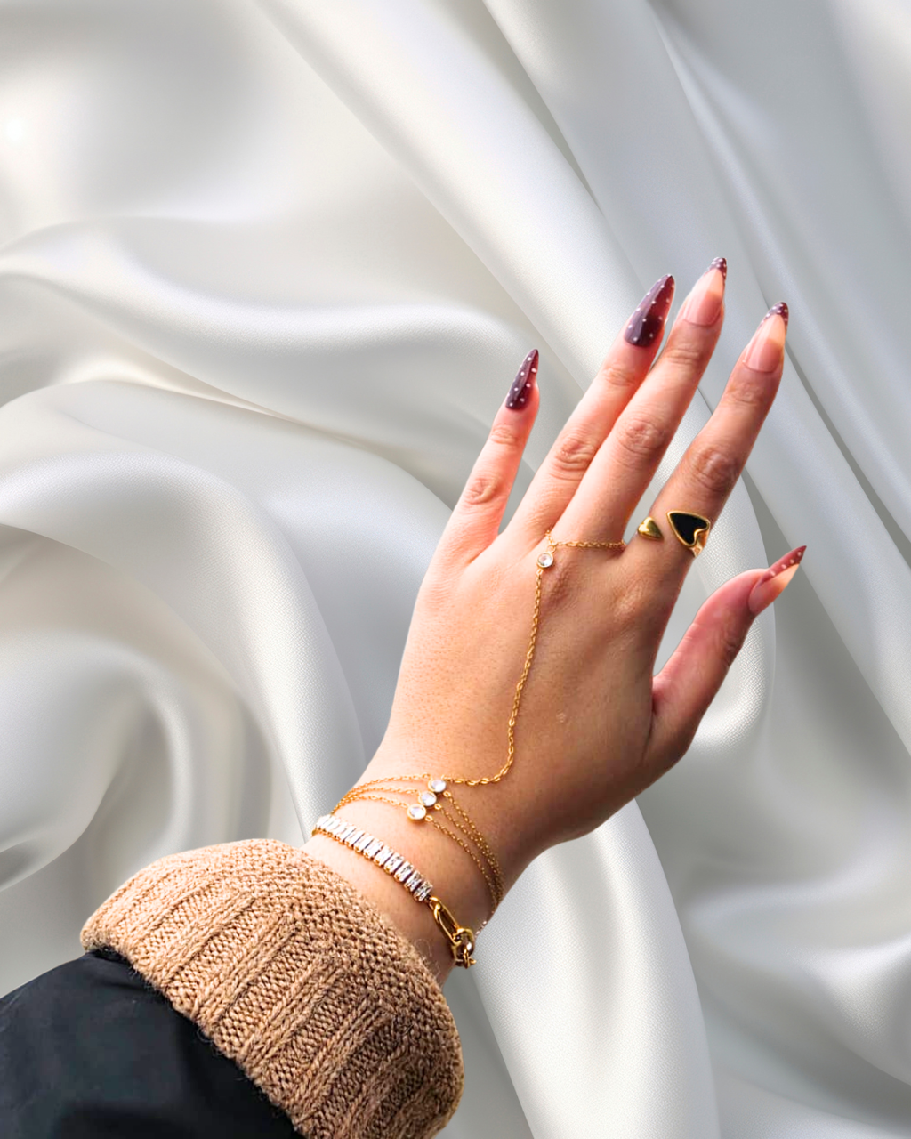 Hand with gold jewelry against a white satin background