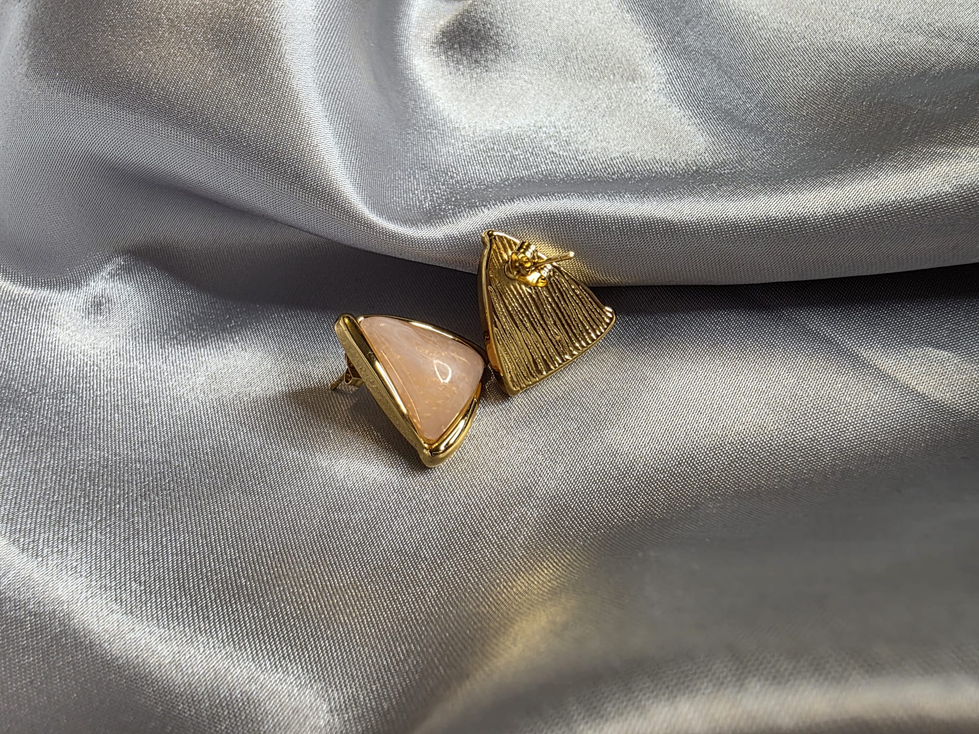 Gold and pink triangle-shaped earrings on a gray fabric background