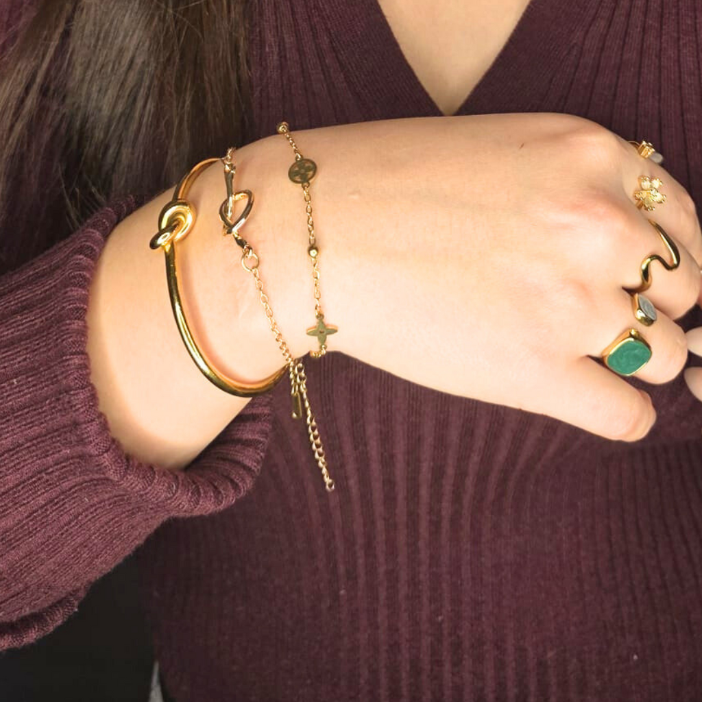 Close-up of a person's wrist wearing gold bracelets and rings on a dark background