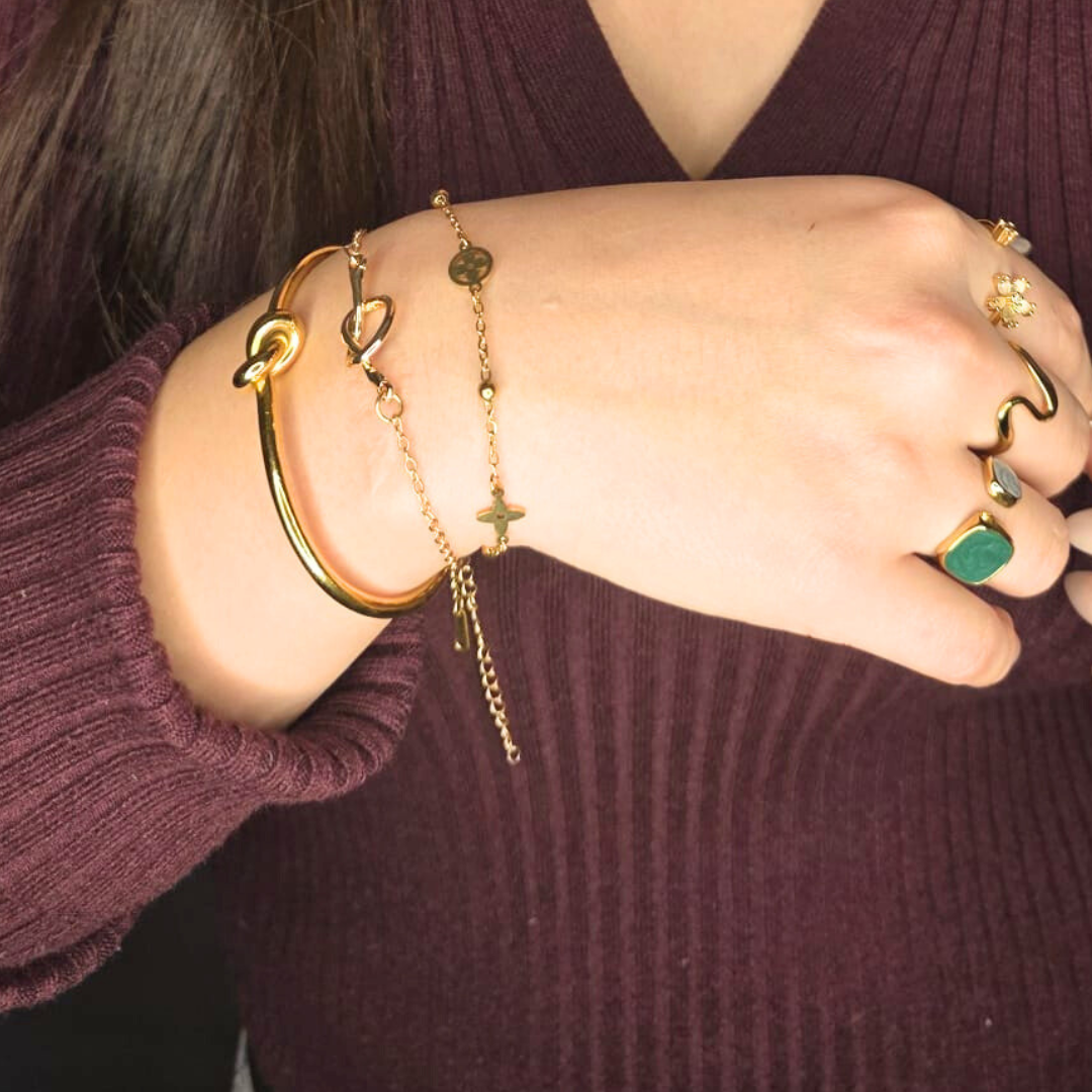 Close-up of a person's wrist wearing gold bracelets and rings on a dark background