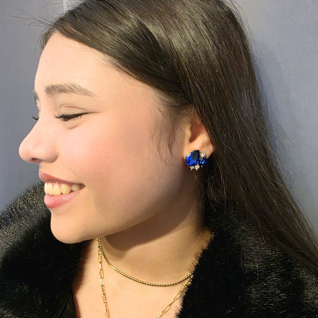 Close-up of a person wearing blue earrings and a necklace with a dark background