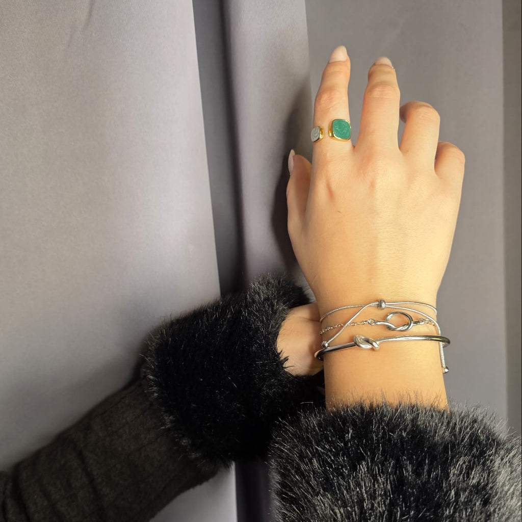 Hand with multiple bracelets and a ring on a neutral background