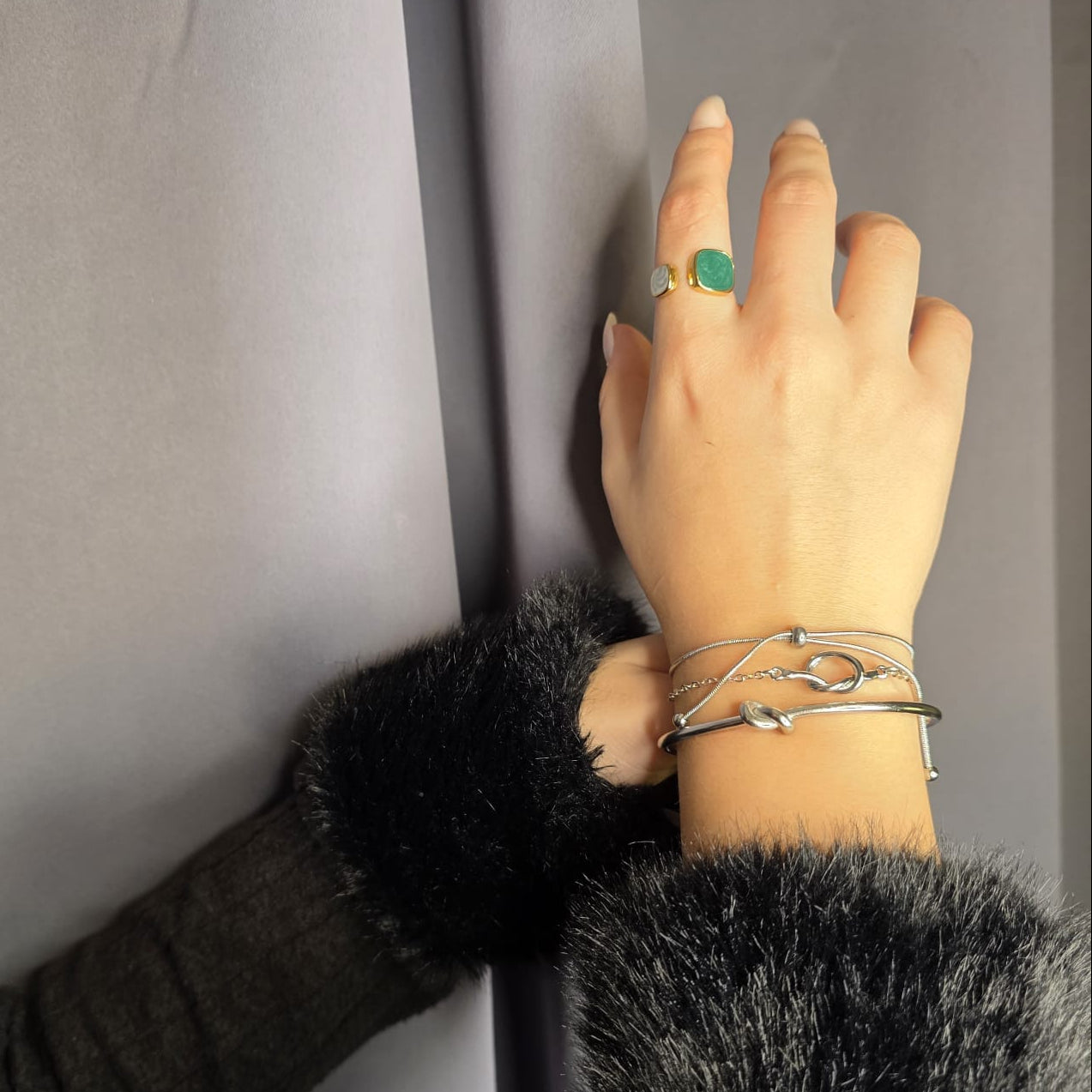 Hand with multiple bracelets and a ring on a neutral background