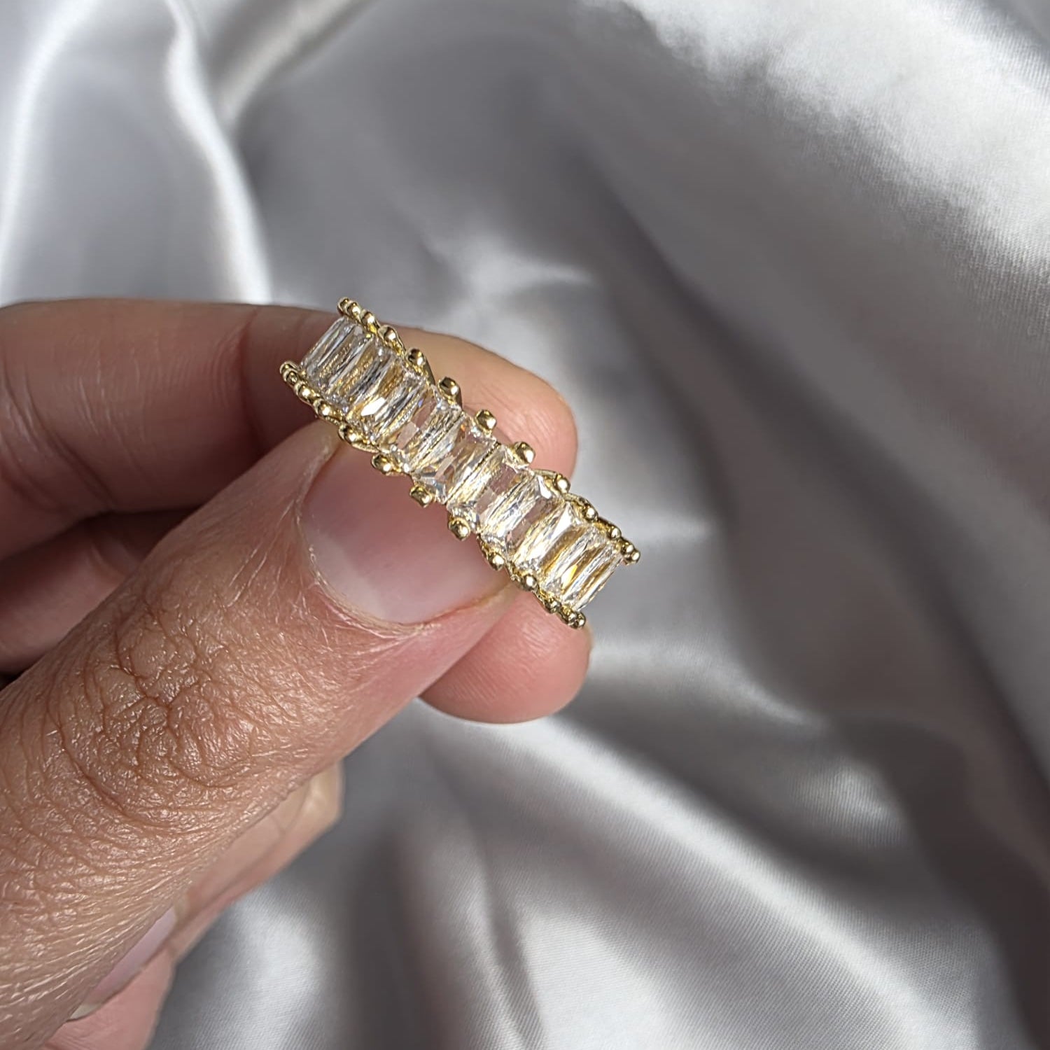 Gold ring with baguette-cut diamonds held by a hand against a silver fabric background