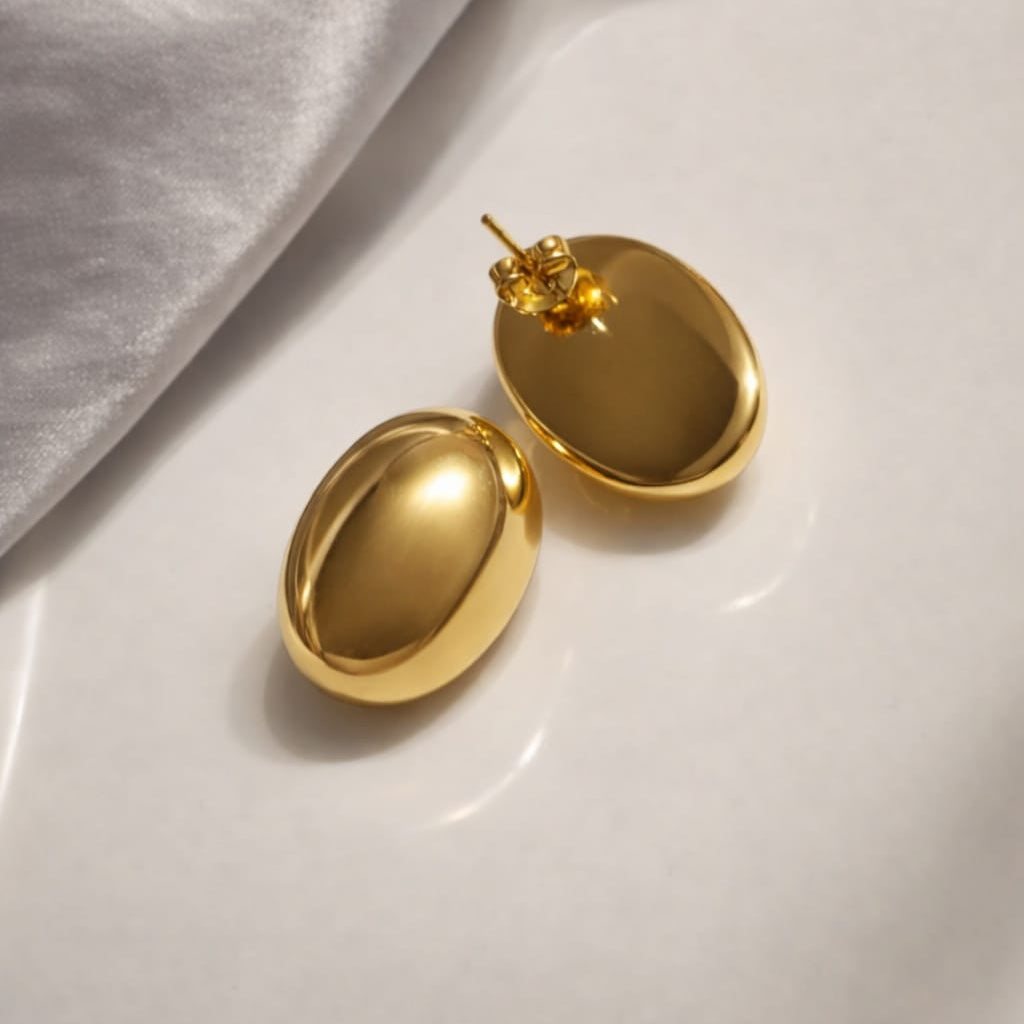 Gold earrings on a white surface with a gray fabric background